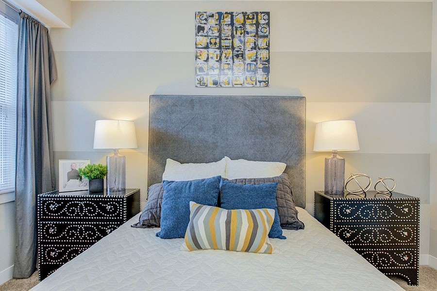 A gray bed with blue pillows and black side tables in a bedroom at Highpointe Apartments.