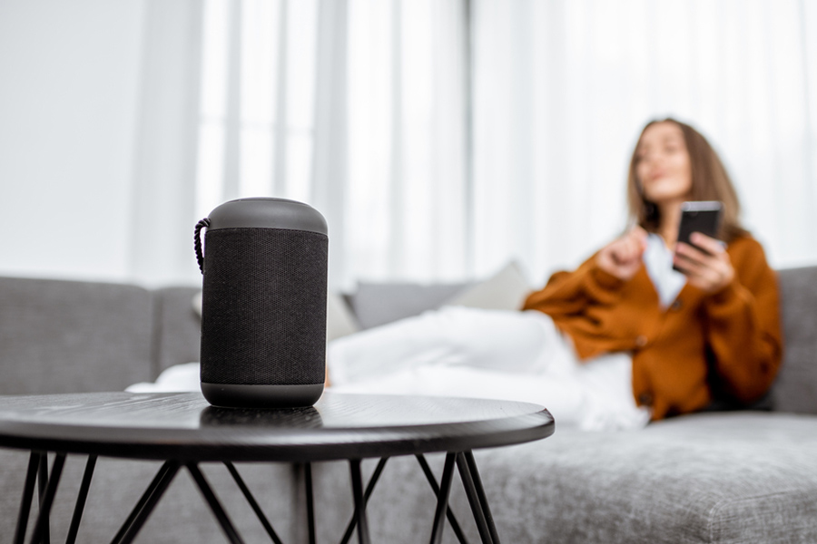Use a smart speaker to conveniently control other devices in your Indianapolis apartment. Woman sitting on a sofa beside a smart speaker on a coffee table